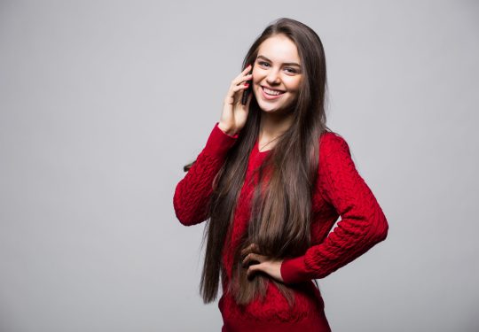 Smiling young woman is pointing on smartphone standing on white background. Smiling woman is pointing on smartphone standing on white background.